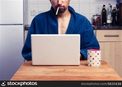 Man in bathrobe smoking and drinking while looking at laptop