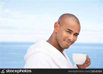 Man in bathrobe with cup of tea in front of ocean head and shoulders