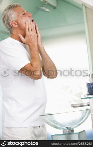Man in bathroom applying aftershave and smiling