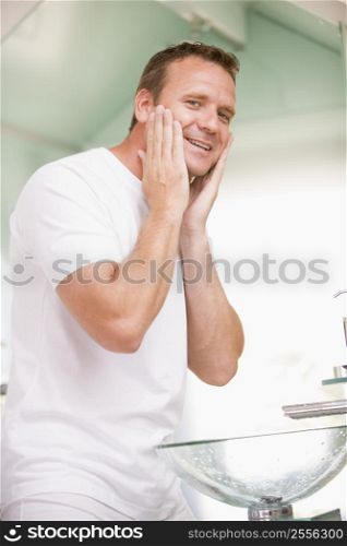 Man in bathroom applying aftershave and smiling