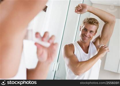 Man in bathroom applying deodorant smiling