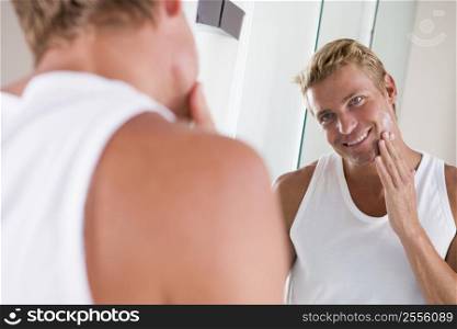 Man in bathroom applying face cream smiling