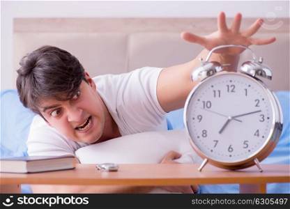 Man in bed frustrated suffering from insomnia with an alarm cloc. Man in bed frustrated suffering from insomnia with an alarm clock