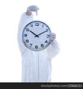 Man in biohazard suit holding clock in front of face pointing to clock with finger standing against white background.