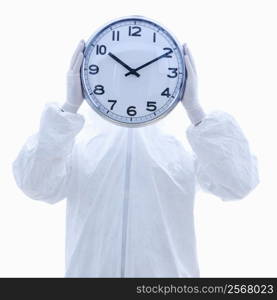Man in biohazard suit holding clock in front of face standing against white background.