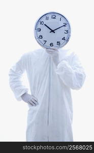 Man in biohazard suit holding clock in front of face standing against white background.