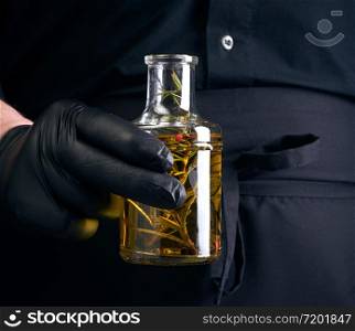 man in black clothes, latex gloves holds a transparent bottle with olive oil, low key, close up
