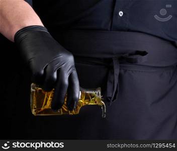 man in black clothes, latex gloves holds a transparent bottle with olive oil, low key