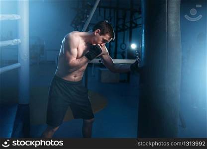 Man in black handwraps exercises with bag in gym. Boxing workout, mens sport. Man in black handwraps exercises with bag in gym