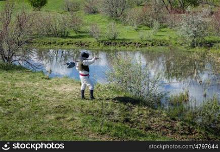 Man in black hat with a stick standing on the river bank