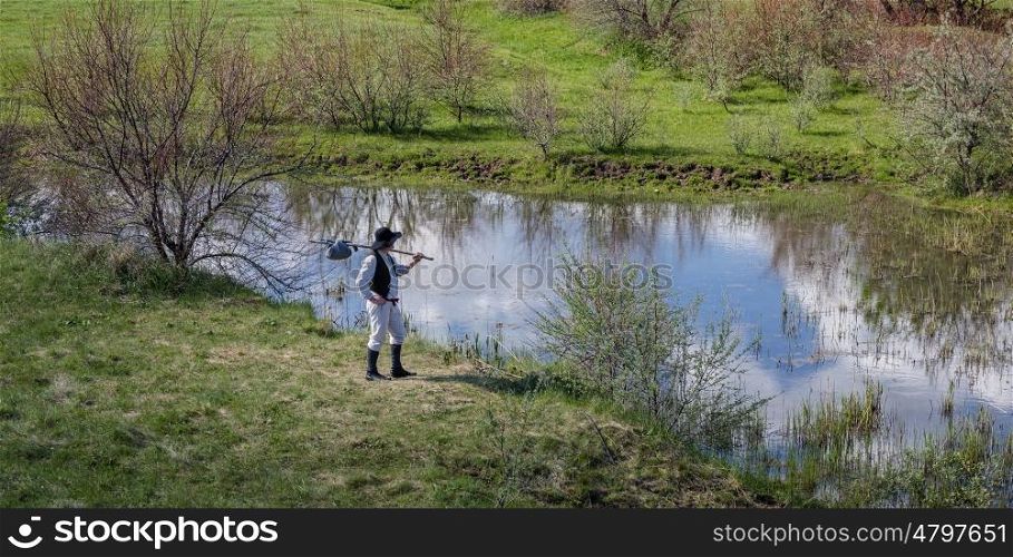 Man in black hat with a stick standing on the river bank