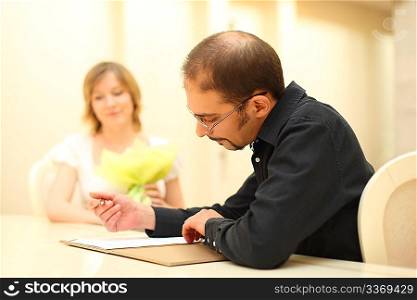 man in black shirt making sign on wedding documents, bride on background