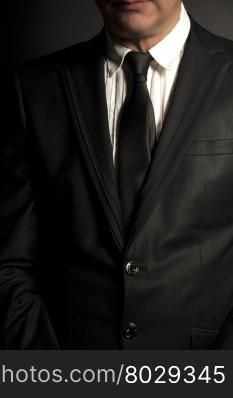 Man in black suit and black tie on a black background