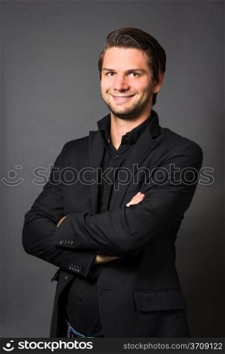 Man in Black Suit in front of a grey background looking happy