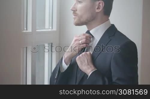 Man in black suit tying tie, groom, businessman concept