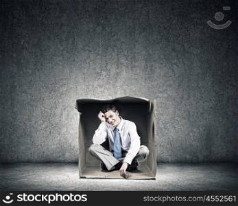 Man in box. Young frustrated businessman sitting in small carton box