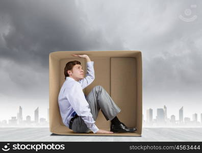 Man in box. Young frustrated businessman sitting in small carton box