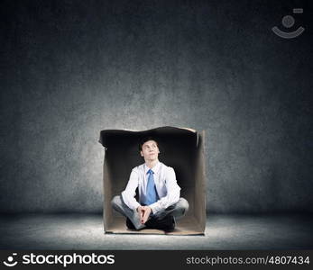 Man in box. Young frustrated businessman sitting in small carton box