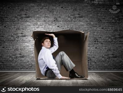 Man in box. Young frustrated businessman sitting in small carton box