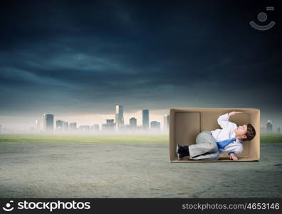 Man in box. Young frustrated businessman trapped in small carton box