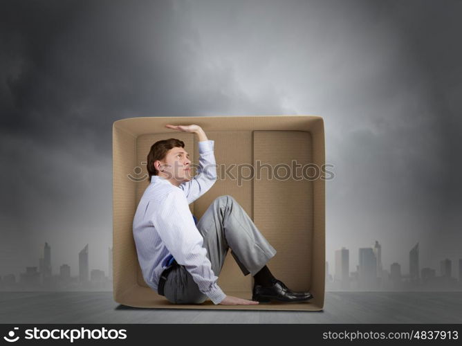 Man in box. Young frustrated businessman trapped in small carton box