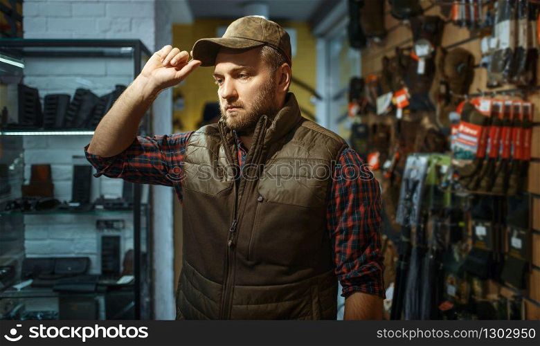 Man in cap, gun shop interior on background. Euqipment and rifles on stand in weapon store, hunting and sport shooting hobby. Man in cap, gun shop interior on background