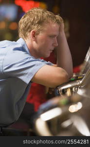 Man in casino playing slot machine frustrated with people in background (selective focus)