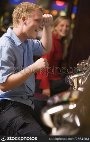 Man in casino playing slot machine smiling with people in background (selective focus)