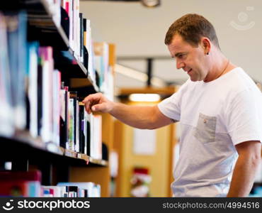 Man in casual wear in library choosing books. Man in library