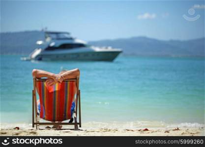 Man in chaise lounge. Man relaxing in chaise lounge on beach and looking at yacht