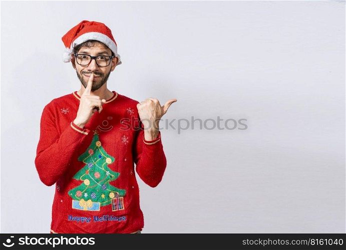 Man in Christmas sweater in silence gesture pointing to the side, Guy in Christmas hat with finger on lips pointing side. Bearded man in christmas hat in silence gesture pointing promo