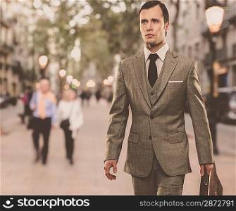 Man in classic grey suit with briefcase walking outdoors