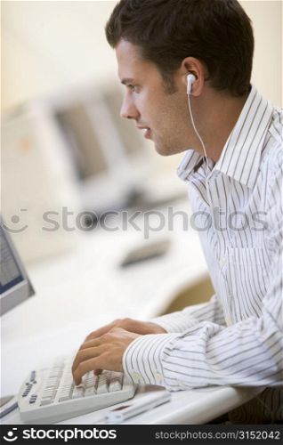 Man in computer room listening to MP3 player while typing