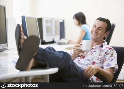 Man in computer room with feet up drinking coffee and smiling