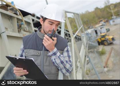 Man in construction site with clipboard and walkie talkie