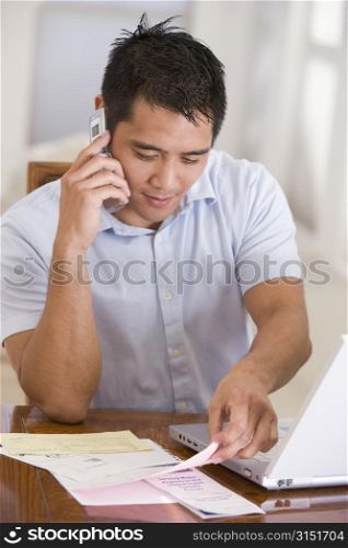 Man in dining room on cellular phone using laptop