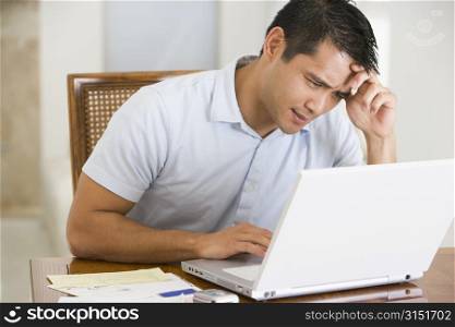 Man in dining room using laptop and frowning