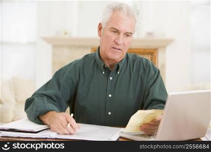 Man in dining room with laptop and paperwork looking unhappy