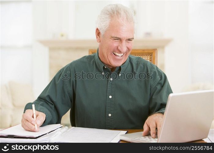 Man in dining room with laptop and paperwork smiling