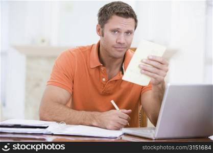 Man in dining room with laptop holding paperwork