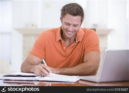 Man in dining room with laptop writing and smiling