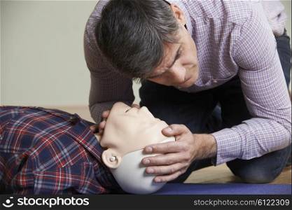 Man In First Aid Class Checking Airway On CPR Dummy