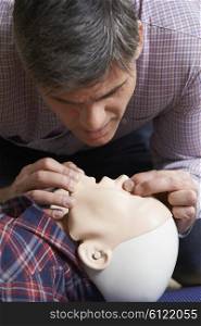 Man In First Aid Class Performing Mouth To Mouth Resuscitation On Dummy