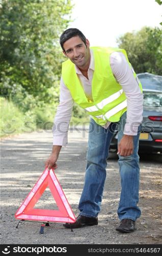 Man in fluorescent vest putting out a warning triangle by a breakdown