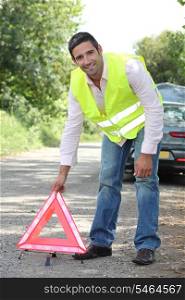Man in fluorescent vest putting out a warning triangle by a breakdown