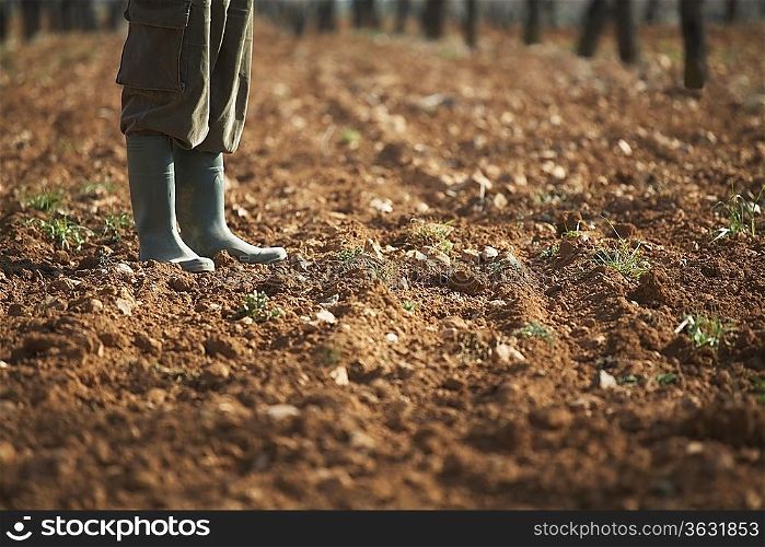 Man in galoshes standing on brown soil, low section