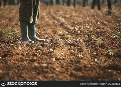Man in galoshes standing on brown soil, low section