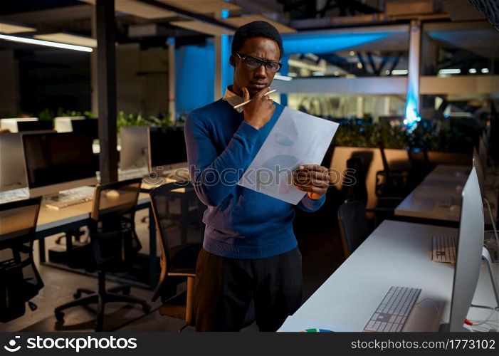 Man in glasses looks at the charts, office lifestyle. Male person at laptop, dark interior on background, modern workplace. Man in glasses looks at charts, office lifestyle