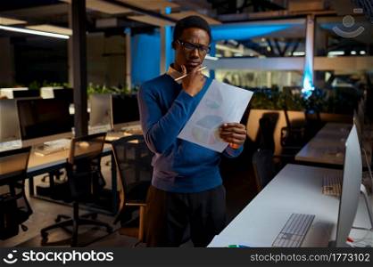Man in glasses looks at the charts, office lifestyle. Male person at laptop, dark interior on background, modern workplace. Man in glasses looks at charts, office lifestyle
