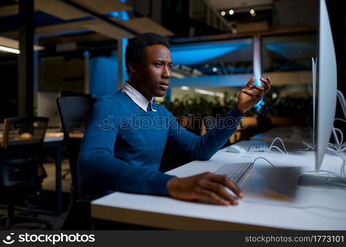 Man in glasses works on computer, office lifestyle. Male person at desktop, dark interior, modern workplace. Man in glasses works on computer, office lifestyle